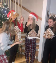 three girls in pajamas and santa hats are holding christmas gifts while one girl holds a gingerbread house