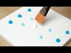 a paintbrush is being used to paint water drops on a white board with blue and orange tips