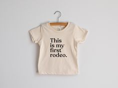 "\"This Is My First Rodeo\" For the newest little ones! Playful modern typography in crisp black ink makes for a humorous statement for new little babies. All artwork is original and professionally screen-printed by hand with care on a super soft 100% organic cotton tee. Shirt color is a natural unbleached off-white color with black ink. This super-soft tee was designed with love and screen printed by hand in-house.  Sizes available in: * 3-6 Months * 6-12 Months * 12-18 Months * 18-24 Months Pl Holiday Photo Shoot, My First Rodeo, Holiday Photoshoot, Sweet Tee, First Rodeo, Usa Baby, Baby Graphic Tees, Baby Top, Baby It's Cold Outside