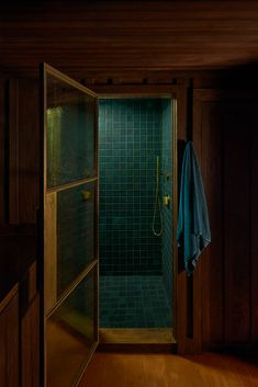 an open door leading into a bathroom with green tile and wooden walls, along with a blue towel hanging on the wall