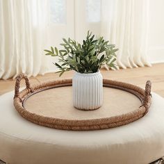 a white vase sitting on top of a round ottoman next to a plant in a pot