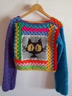 a crocheted sweater with a cat on it hanging from a wooden hanger