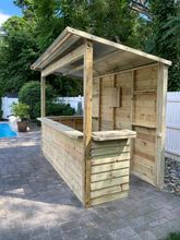 a small wooden bar in the middle of a brick patio next to a swimming pool