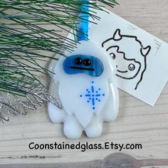 a blue and white brooch sitting on top of a wooden table next to a pine tree