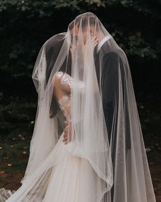 a bride and groom kissing in front of some trees with their veils pulled back