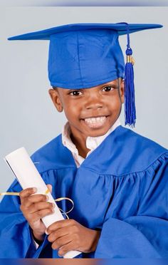 a young boy wearing a blue graduation gown and holding a white piece of paper in his hand