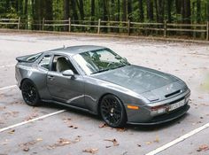 a silver sports car parked in a parking lot next to trees and leaves on the ground