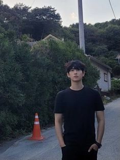 a man standing in the middle of a road next to an orange cone and trees