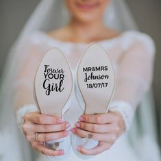 the bride is holding her wedding shoes with their names printed on them, and they are both wearing white slippers