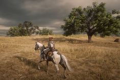 a man riding on the back of a white horse across a dry grass covered field