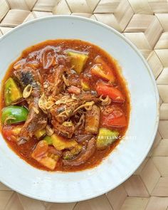 a white bowl filled with stew on top of a woven place mat next to a spoon