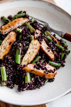 a white plate topped with rice and meat next to green beans on top of a wooden table