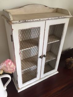 an old china cabinet with chicken wire on the doors and shelves, next to a pink flower