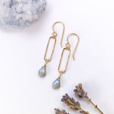 two pairs of earrings sitting next to each other on top of a rock and lavender flowers