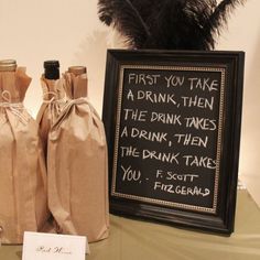 two wine bottles are sitting on a table next to a sign that says first you take a drink then the drink takes the drink