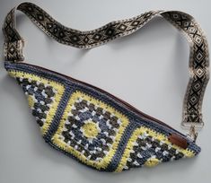 a crocheted purse is hanging on a white wall with a brown leather strap