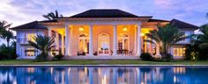 a large house with a pool in front of it at dusk or dawn, surrounded by palm trees