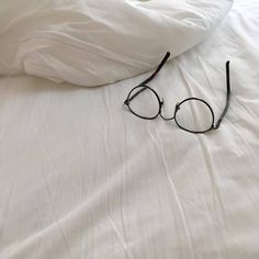 a pair of glasses laying on top of a white comforter next to a pillow