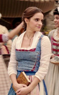 a woman dressed in an old fashioned dress and holding a book while standing next to other women