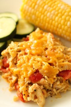 a white plate topped with chicken and veggies next to corn on the cob