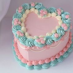 a heart shaped cake with pastel frosting and flowers on top, sitting on a white surface