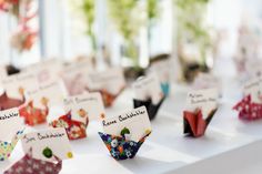 there are many small origami flowers on the table with name tags attached to them