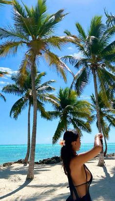 a woman standing on top of a sandy beach next to palm trees