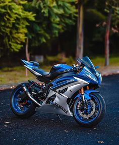 a blue and silver motorcycle parked on the side of a road next to some trees