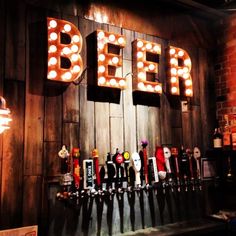 beer taps lined up in front of a wooden wall with light bulbs on it's sides