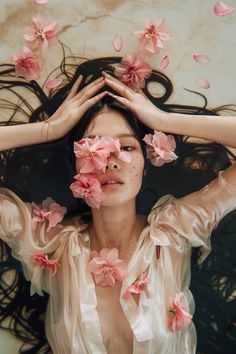 a woman with her hands on her head surrounded by pink flowers and hair flying in the air