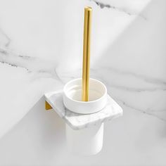 a white marble bathroom with a gold colored toilet brush