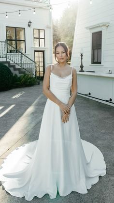 a woman standing in front of a white house wearing a wedding dress and holding her hand on her hip