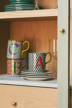 some cups and plates are sitting on the shelf in front of each other with letters painted on them