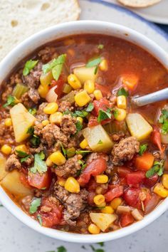 a white bowl filled with meat and vegetables next to some pita bread on the side