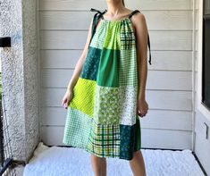 a woman standing in front of a house wearing a dress made out of patchwork fabric