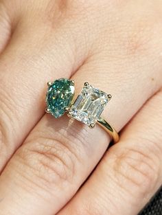 a woman's engagement ring with an emerald and diamond center stone on her finger