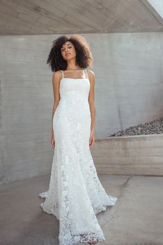 a woman standing in front of a wall wearing a white dress