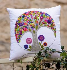 a white pillow with a colorful tree design on it sitting next to a potted plant