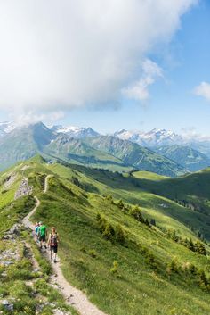 two people walking up a trail on top of a hill with mountains in the background