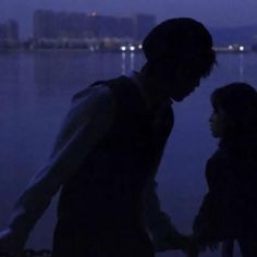 a man and woman standing next to each other in front of the water at night