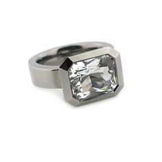 This ring has a 12mm x 10mm custom radiant cut, rock crystal which is approximately 5 carats. It is bezel set in polished silver with black rhodium finish. The shank is solid and measures 5.5mm wide at the top by 3.5mm deep and tapers down to 2.25mm deep. It is available as a standard in full, half sizes in 6-9 and available in other sizes as a special request. It is also available in green amethyst, lavender amethyst, and blue topaz. Dimensions: Bezel 12.75mm long x 15.75mm wide x 8.75mm deep A Modern White Gold Rings With Rectangular Stone, Modern White Gold Ring With Rectangular Stone, Modern Large Stone Jewelry For Formal Occasions, Modern Rings With Large Stone For Formal Events, Modern Rings With Large Stone For Formal Occasions, Modern Octagon Jewelry With Bezel Setting, Modern White Gold Octagon Ring, Modern Rectangular Jewelry With Bezel Setting, Modern Radiant Cut Bezel Set Rings