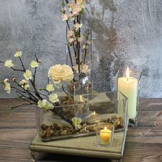 flowers and rocks are arranged in glass vases on a wooden table next to a candle