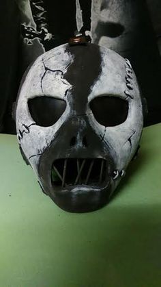 a black and white mask with holes in the middle on a green surface, next to a pair of scissors