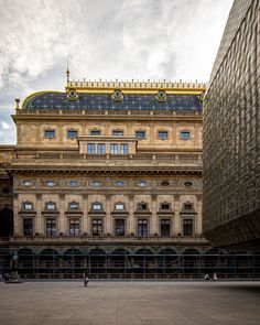 a large building with many windows and people walking around in front of it on a cloudy day