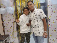 two men standing next to each other in front of balloons and streamers on the wall