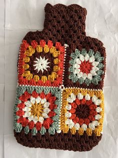 a crocheted pot holder is sitting on a white tablecloth covered with brown, green, yellow and red squares