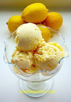 three scoops of ice cream sit in a glass bowl with lemons behind it