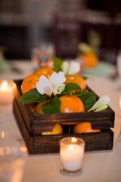 a wooden box filled with oranges and flowers on top of a table next to candles