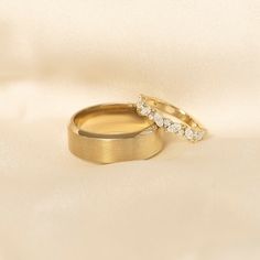 two gold wedding rings with diamond accents on a white satin background in close up view