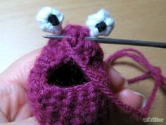 a hand holding a crocheted object with two eyes on it and a needle in the middle